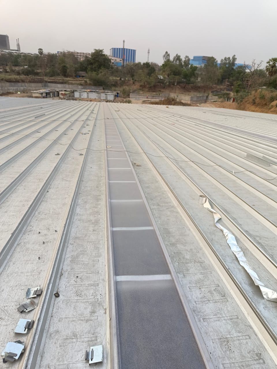 Steel roofing clips laid out along a purlin next to newly laid sheets and a skylight