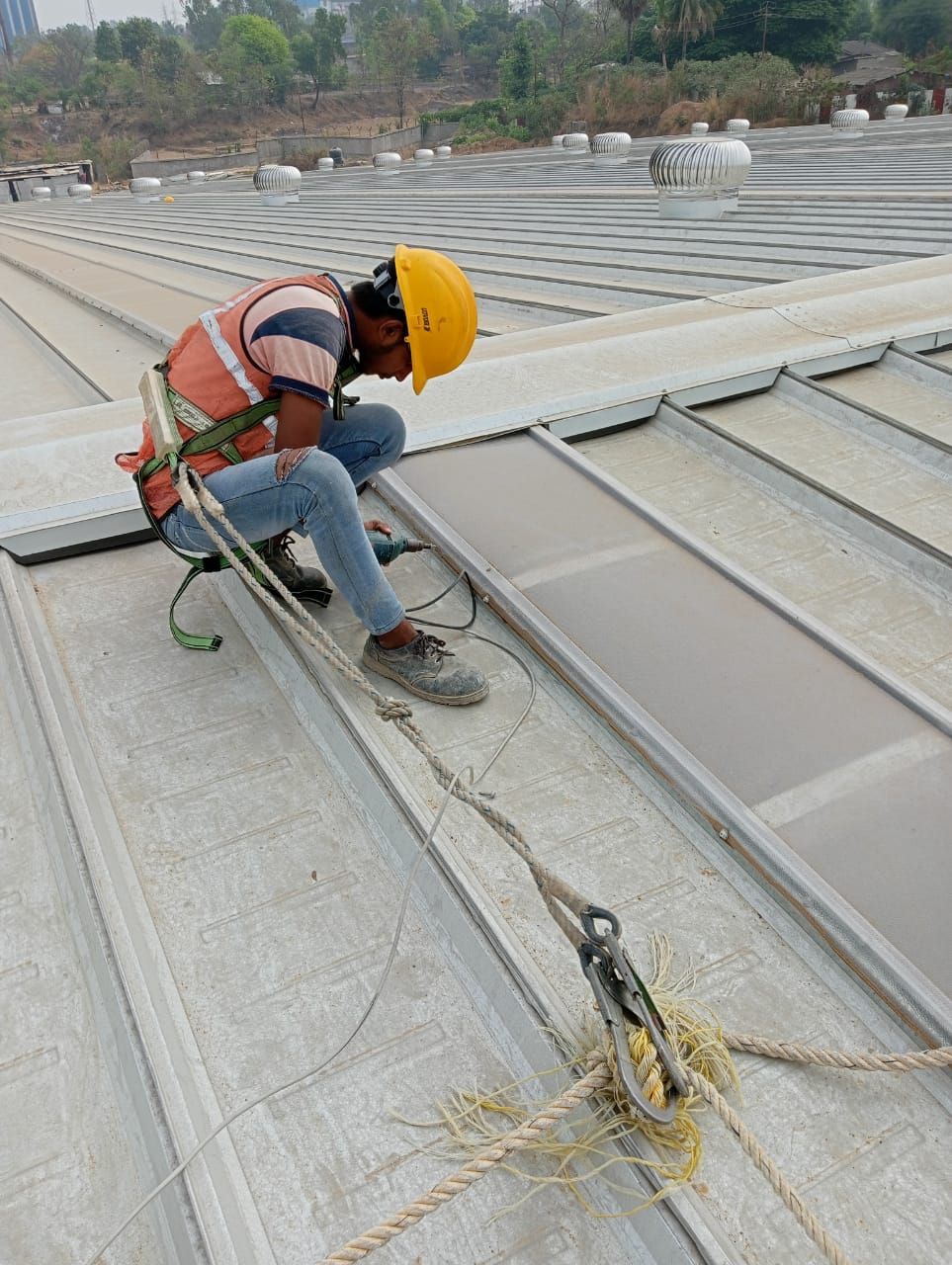 Roofer in a helmet and full-body harness fixing a ridge flashing, tied to a lifeline