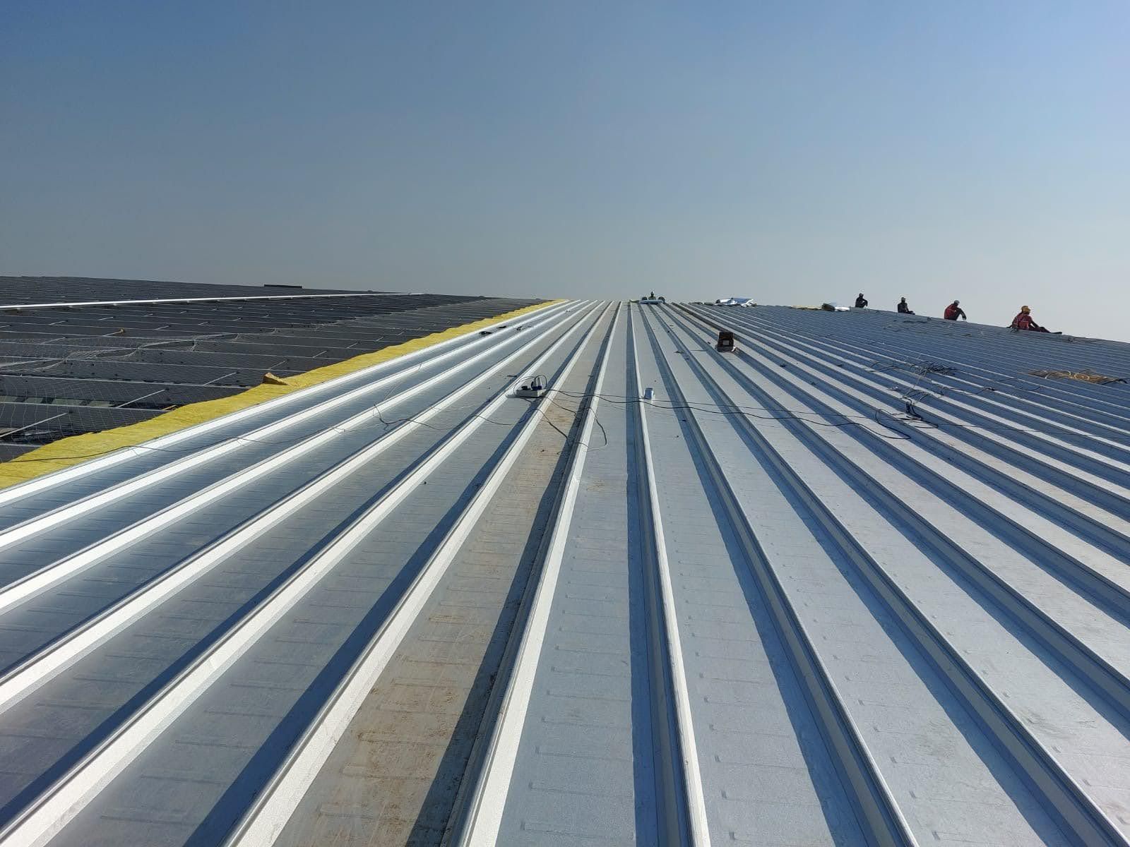 Long run of clip lock roof sheeting on a large industrial roof, with installers working at the far end