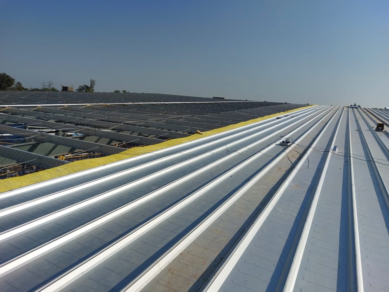 Clip lock roof sheets laid over yellow insulation, with the open roof structure and safety mesh beside them