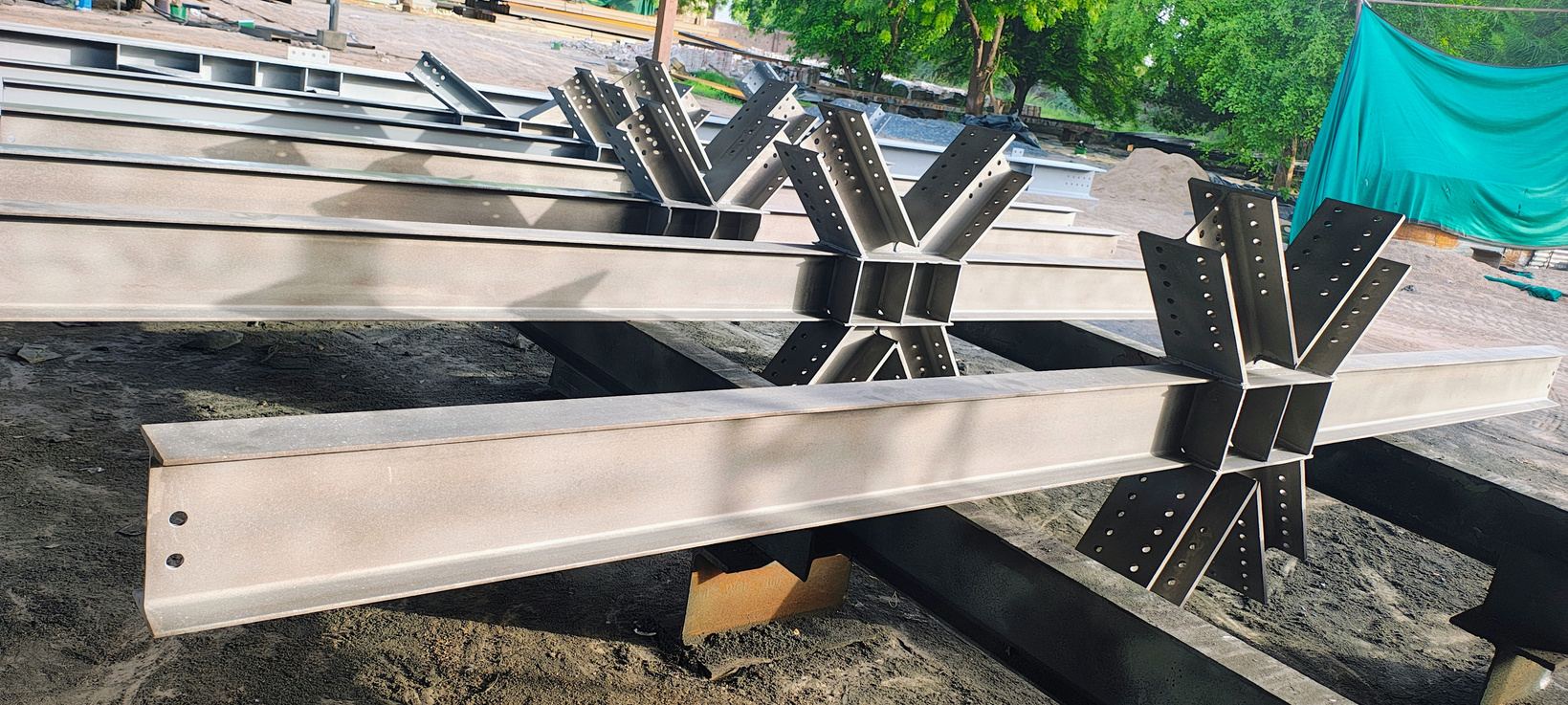 Fabricated steel beams with bolted end plates stacked in a fabrication yard