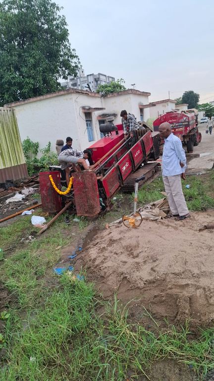 Crew operating a horizontal directional drilling rig to lay cable beside railway buildings