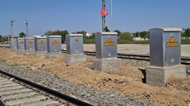 Row of grey signalling location boxes on concrete plinths beside a railway track