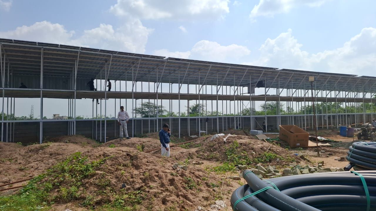 Elevated steel structure carrying rows of solar panels, with engineers inspecting it from the ground
