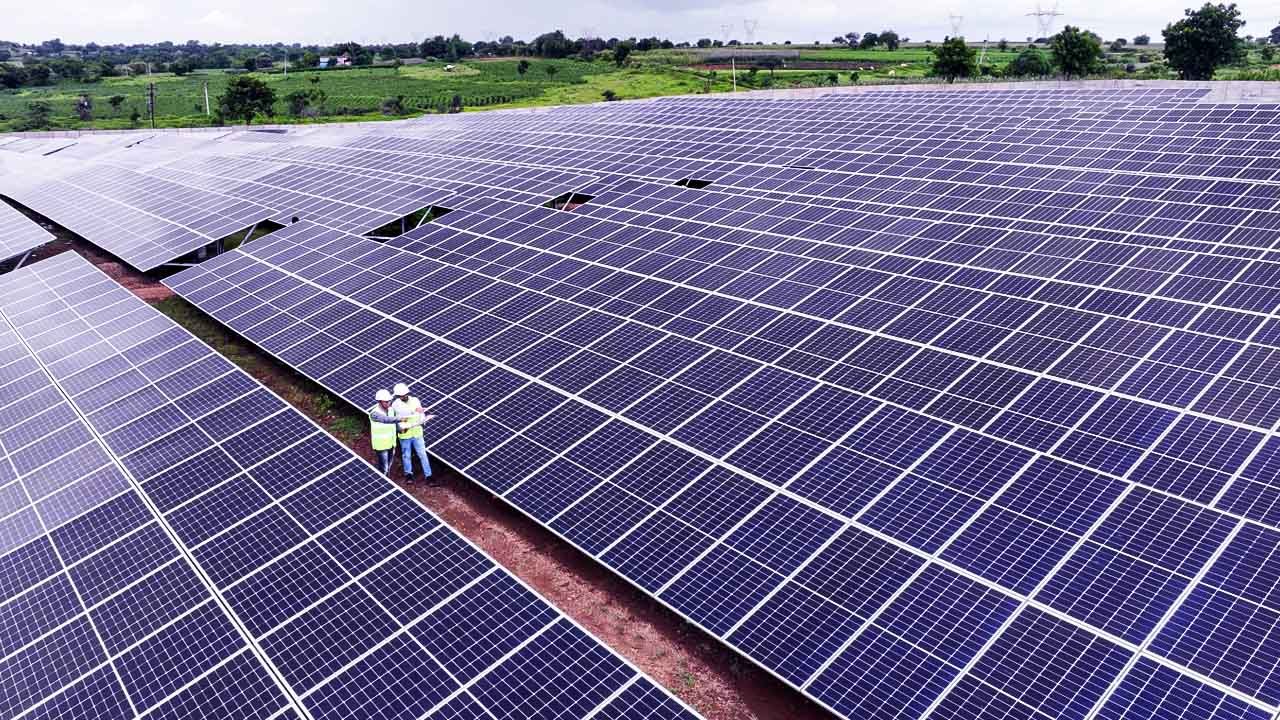 Ground-mount solar plant with long rows of panels and two engineers inspecting them
