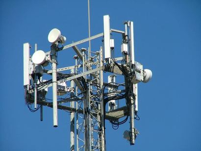 Top of a telecom mast with sector antennas and microwave dishes against a blue sky