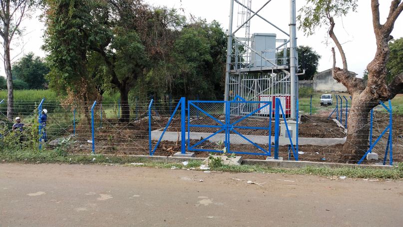 Telecom tower site with blue perimeter fencing and gate beside a road